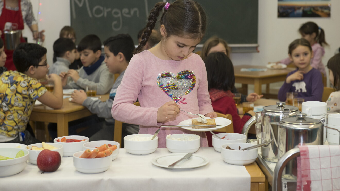 Ein kleines Mädchen in rosa T-Shirt steht an einem Frühstücksbuffet