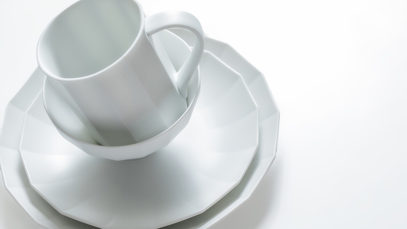多角形のデザインで統一された白い皿とカップが重ねられている