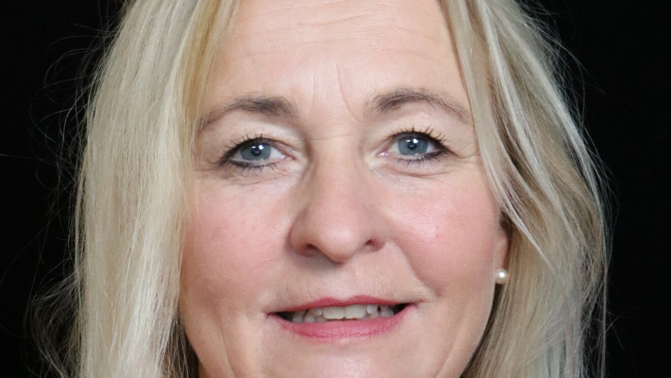 Eine Frau mit blonden Haaren und einer roten Bluse lächelt in die Kamera.