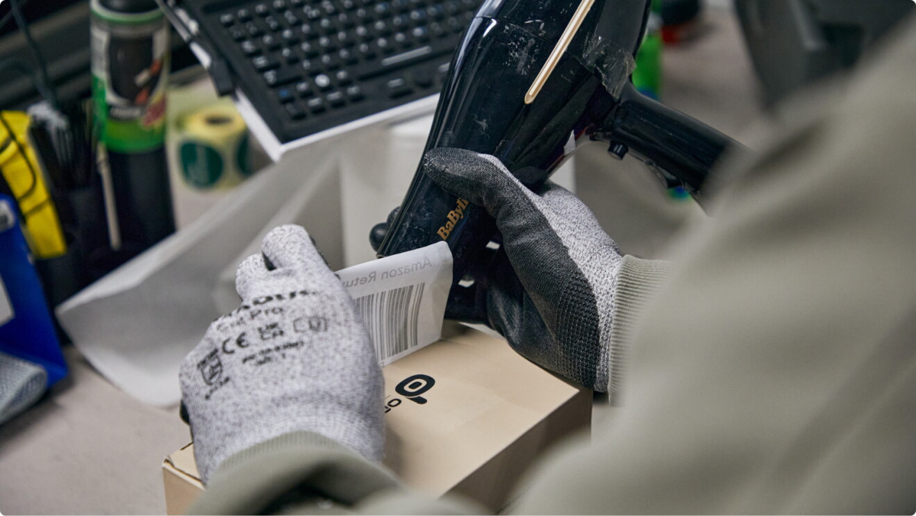 Gloved hand removing barcode label from box using hairdryer heat