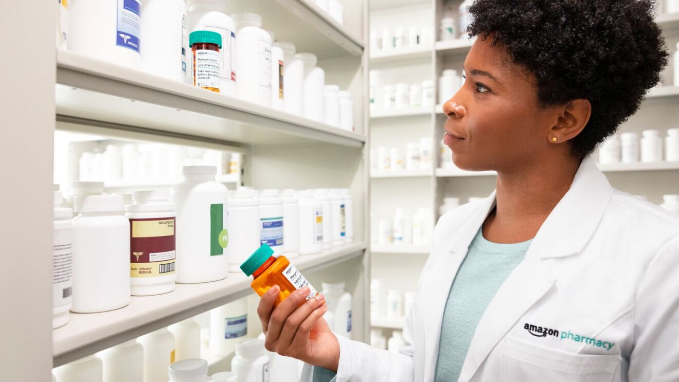 Amazon Pharmacy employee inspecting prescription medication in front of shelves stocked with pharmaceuticals