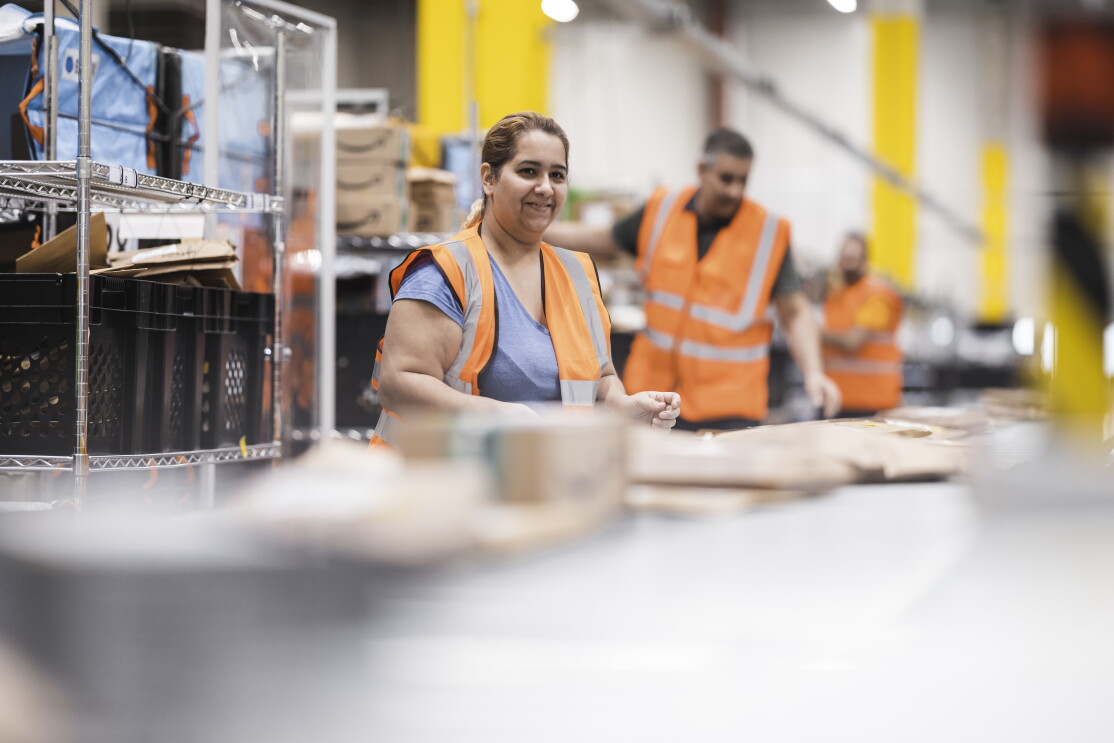 Amazon Mitarbeiterinnen und Mitarbeiter in einem Verteilzentrum bereiten die Päckchen für die Zustellung vor.