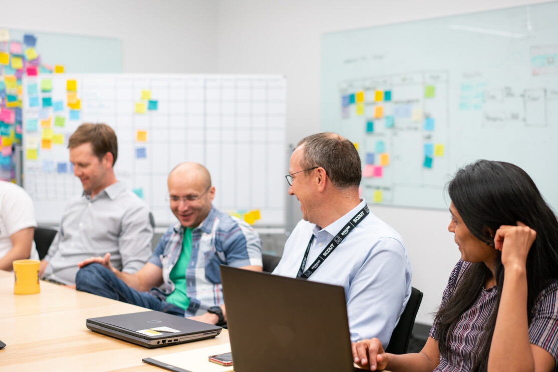 Amazon Scout hardware engineers sit together at a conference table, having a discussion. 
