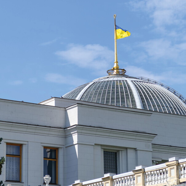 An image of the top of the Ukraine parliament building. There is a Ukraine flag flying at the top of the building.