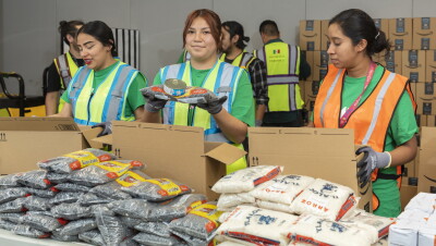 Tres mujeres con chalecos preparando comida para poner en cajas de ayuda ante emergencias. 