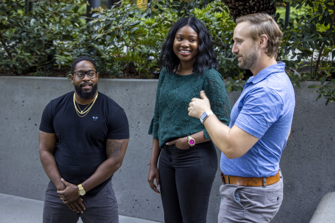 Three people stand together while talking.
