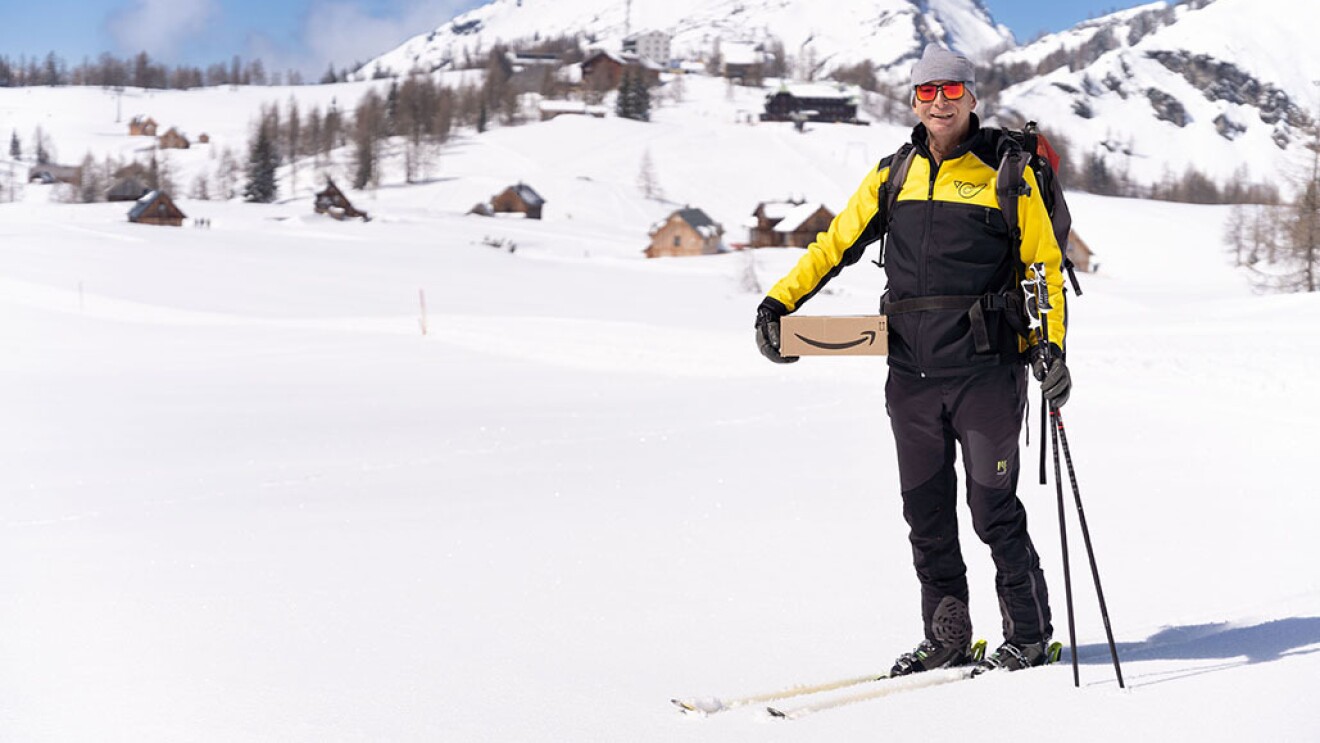Helmut Edelmaier wears his ski gear and holds an Amazon package at the mountan village.