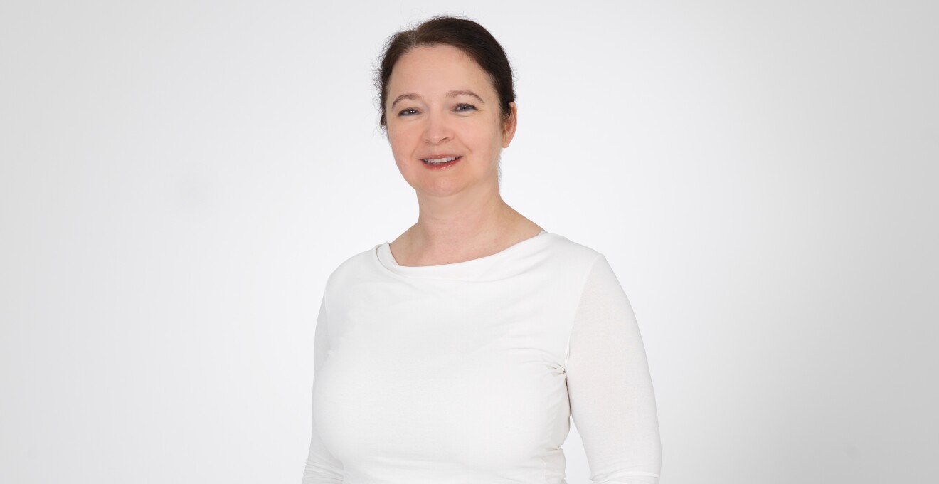 AWS Mitarbeiterin Agnes Balazs mit weißem Oberteil vor einer weißen Wand stehend.