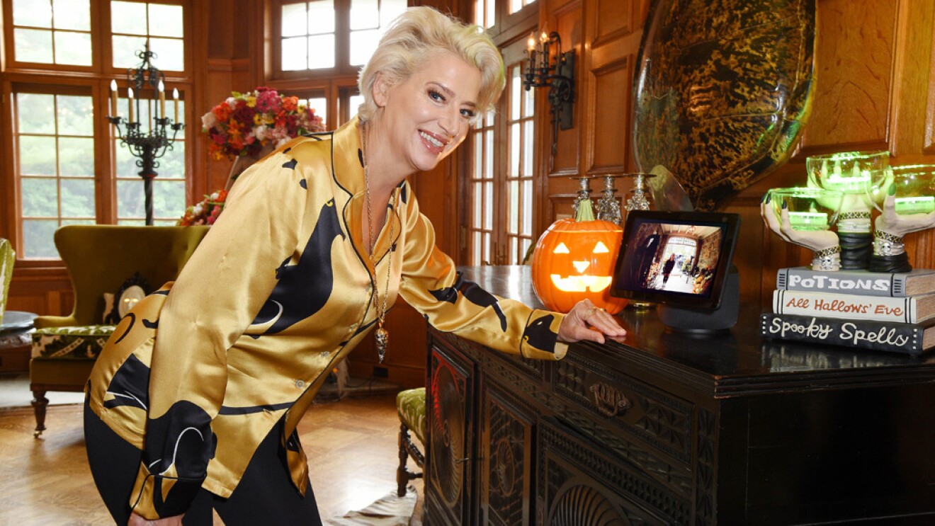 一个女人靠在家里的桌子上。桌子上有一个Echo Show设备,还有万圣节的装饰。