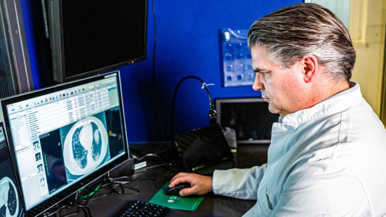 Un uomo siede di fronte allo schermo di un computer che mostra immagini di diagnostica ospedaliera. 
