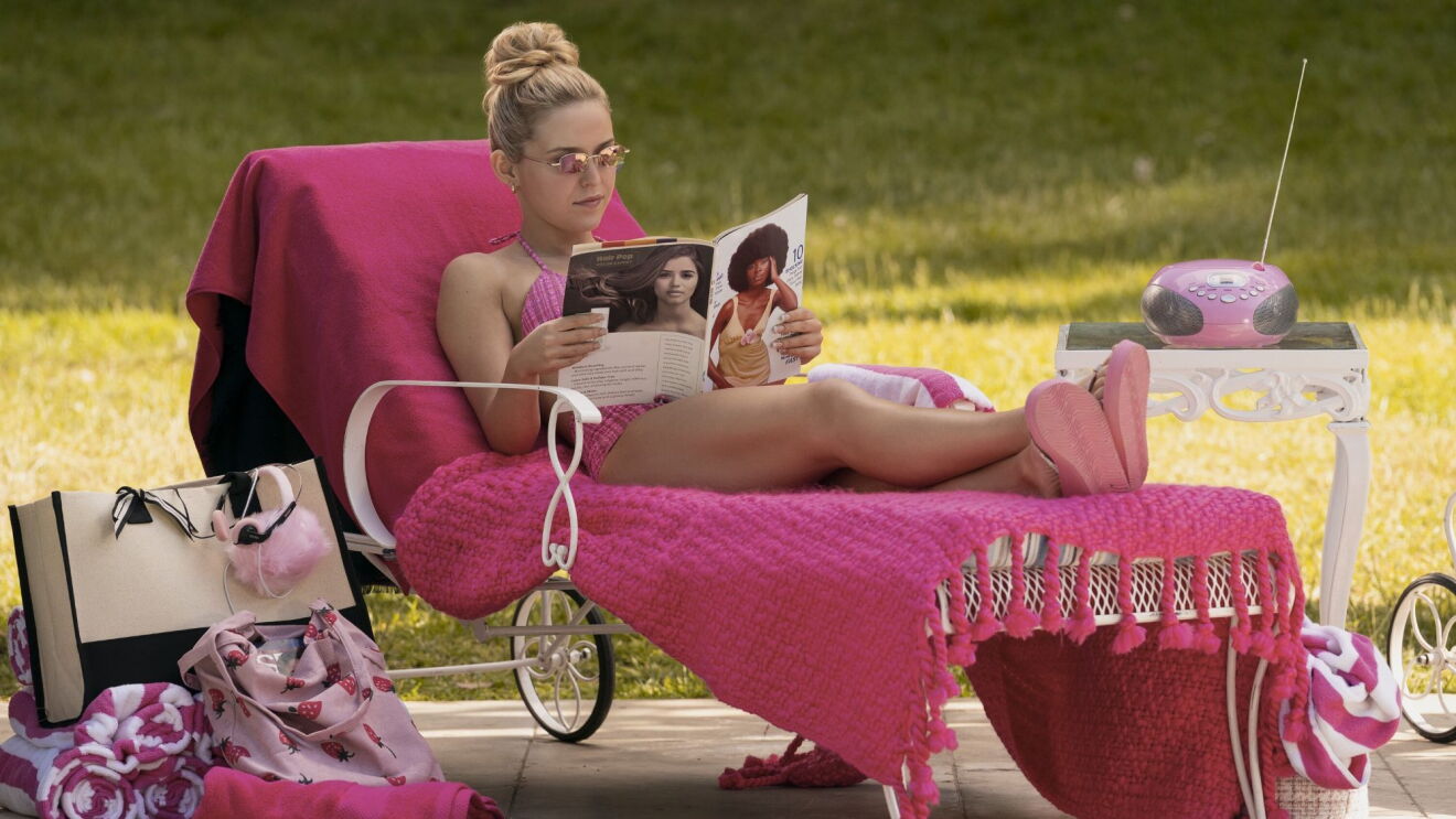 Still image from 'Elle' Season 1, actress in pink bikini reading magazine while lounging on pink chair outdoors with matching accessories