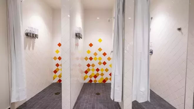 バスアメニティが据え付けられたシャワーブースが3つ並んでいる。その部屋の壁には黄色、赤、そしてオレンジ色の四角いタイルで装飾が施されている