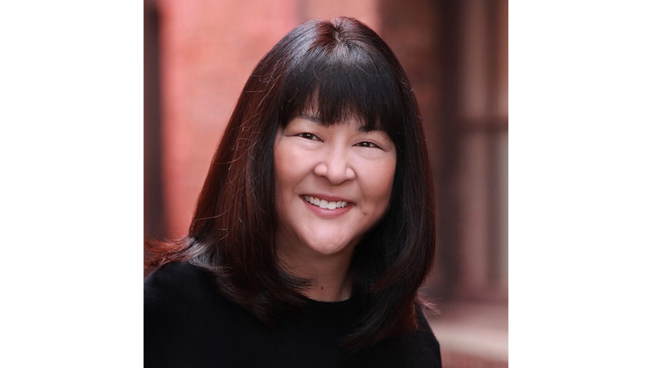 A woman who is Asian wears a black top and smiles at the camera.