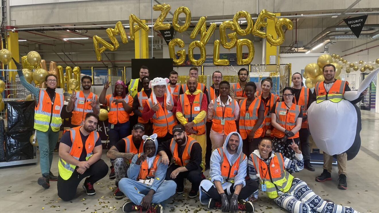 Man sieht eine Gruppe von Amazon Mitarbeiter:innen im Schlafanzug, die vor goldenen Luftballons posieren.