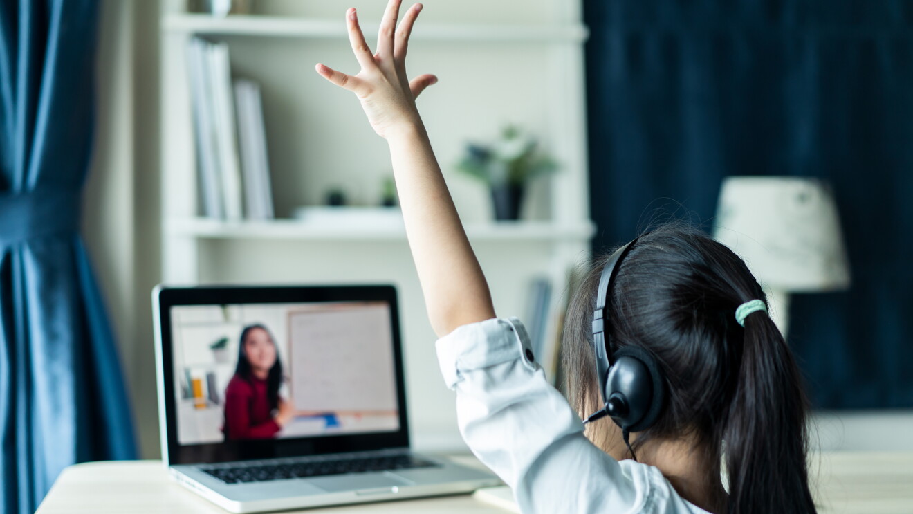 Asian child raising her hand to her teacher via online learning