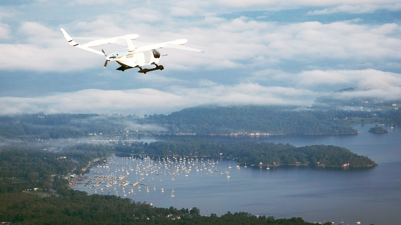 Small aircraft flying over water and land in partly cloudy skies