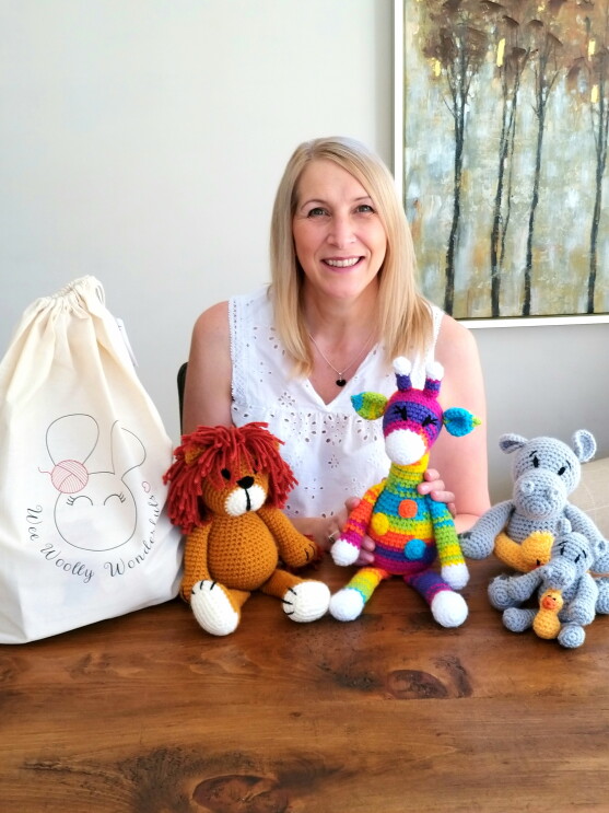 Lisa Dobbs from Wee Woolly Wonderfuls sitting behind some of the toys that she has made using her crochet kits. 