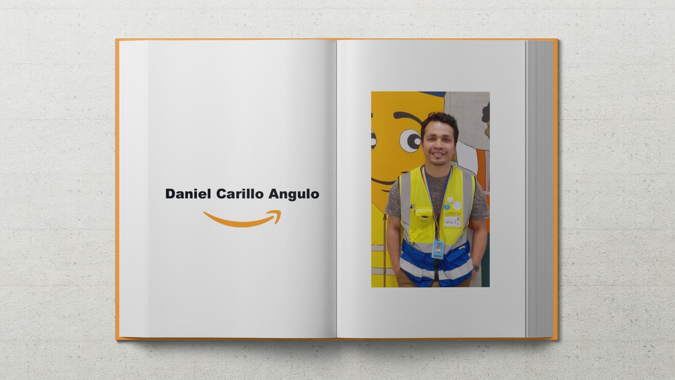 Daniel, ein junger Mann mit braunen lockigen Haaren, lehnt in Sicherheitsweste an einer Wand auf dem das Amazon Maskottchen Peccy abgebildet ist.