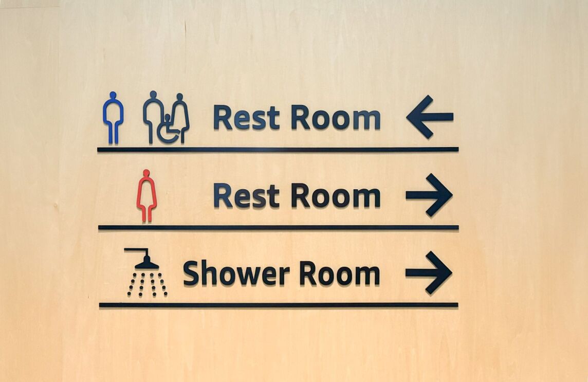 木製の壁に貼られた表示。矢印と男性・女性・車いすなどのマークとRest Room、Shower Roomという文字