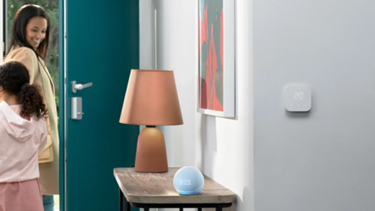 An Amazon Echo device sits on a side table while a mother and daughter exit out of a door