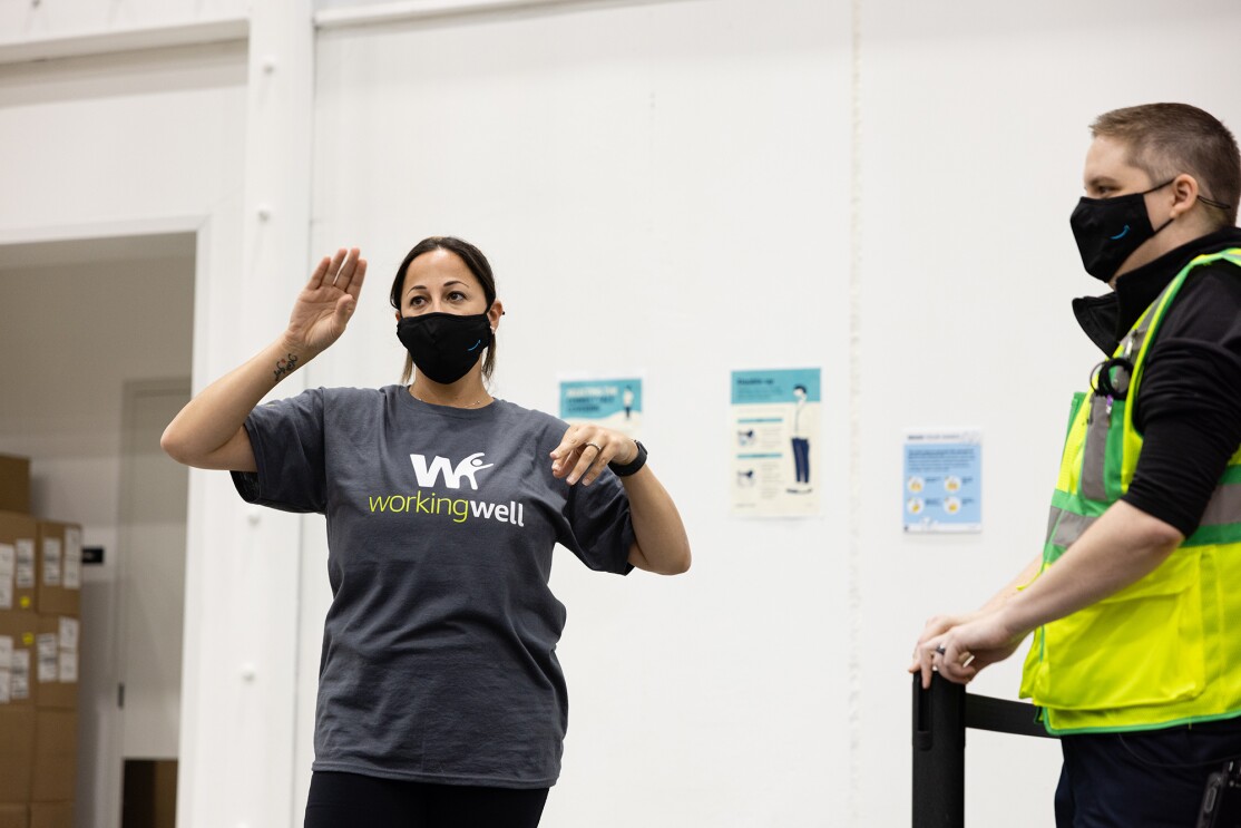 An image of Leila Brown wearing WorkingWell shirt and a mask with the Amazon logo on it as she speaks to employees in her fulfillment center.