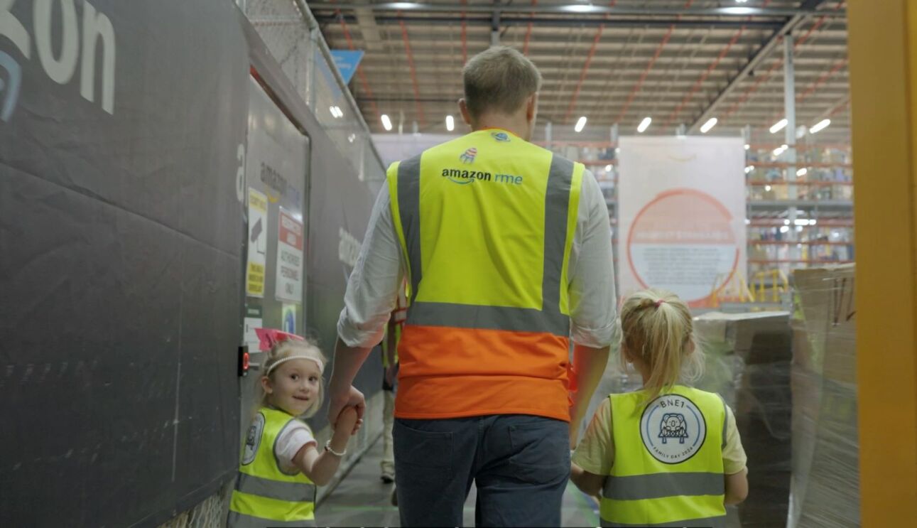 two children guided by a man in Amazon fulfillment centre
