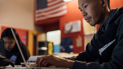 一名学生在笔记本电脑上工作,背景是美国国旗。