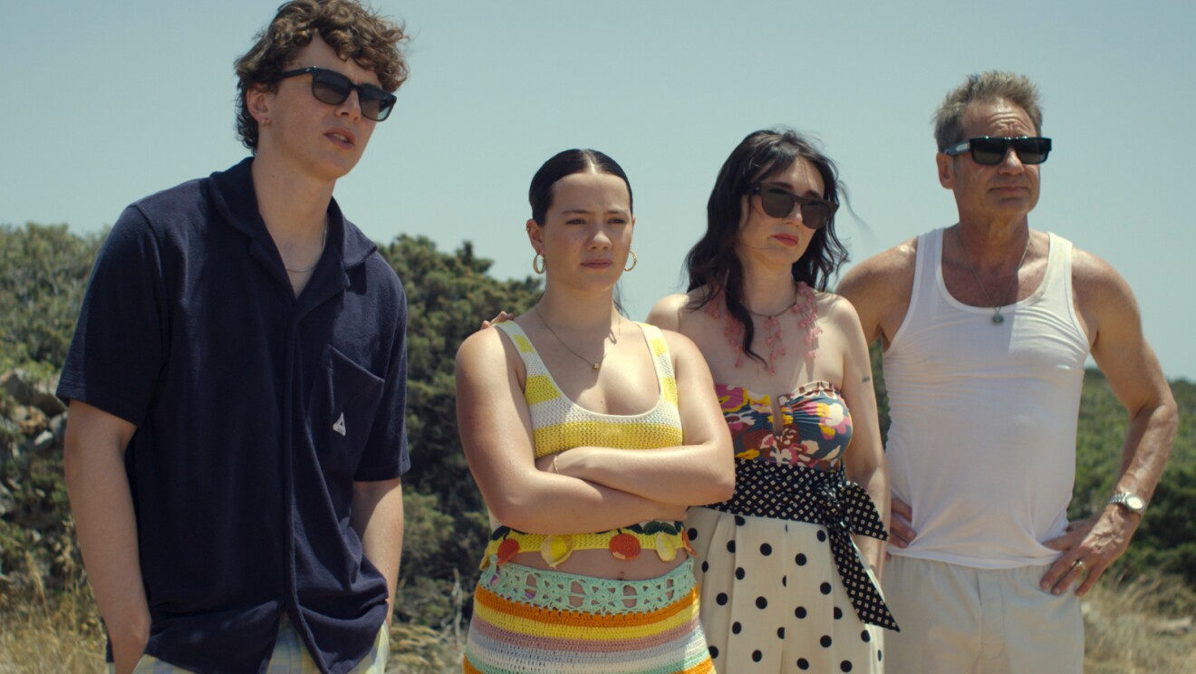 Four people posing outdoors on a sunny day, dressed for warm weather
