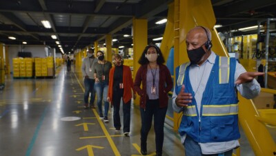 A group of socially-distanced people wearing masks tour an Amazon fulfilment centre.