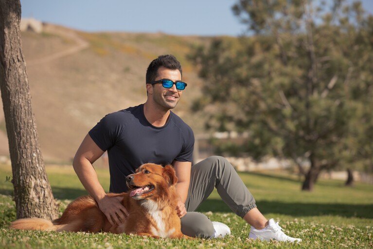 An image of a man sitting in a park with his dog while wearing Echo Frames.