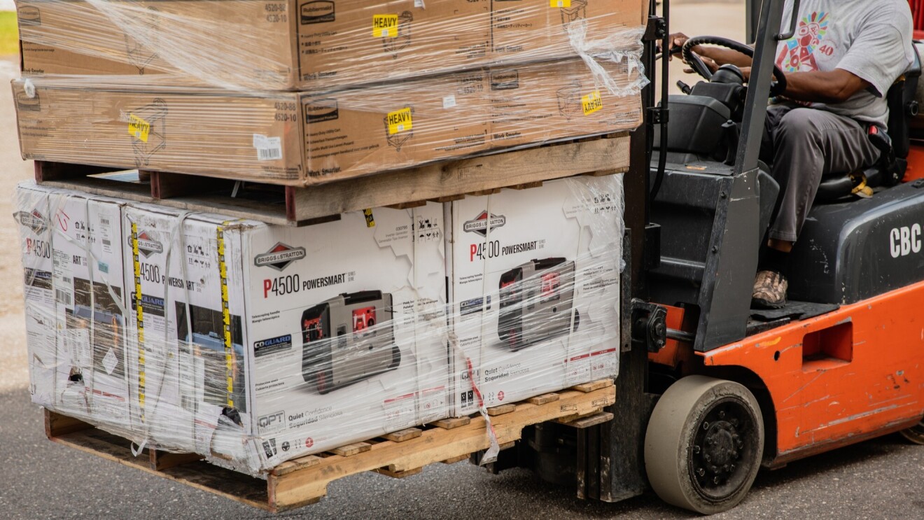 A man working with Amazon's disaster relief team is driving a forklift loaded with generators at the front. These generators will be used to provide power to those affected by recent natural disasters in the U.S.