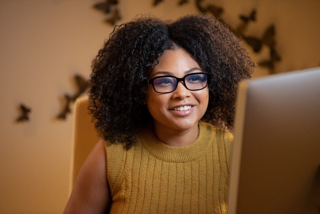 A woman smiles wearing Echo Frames with blue light filtering lenses while looking at her computer screen.