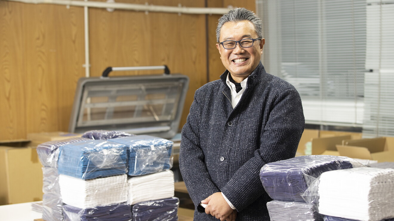 室内でビニール袋に包まれたタオルの後ろに立つ笑顔の男性