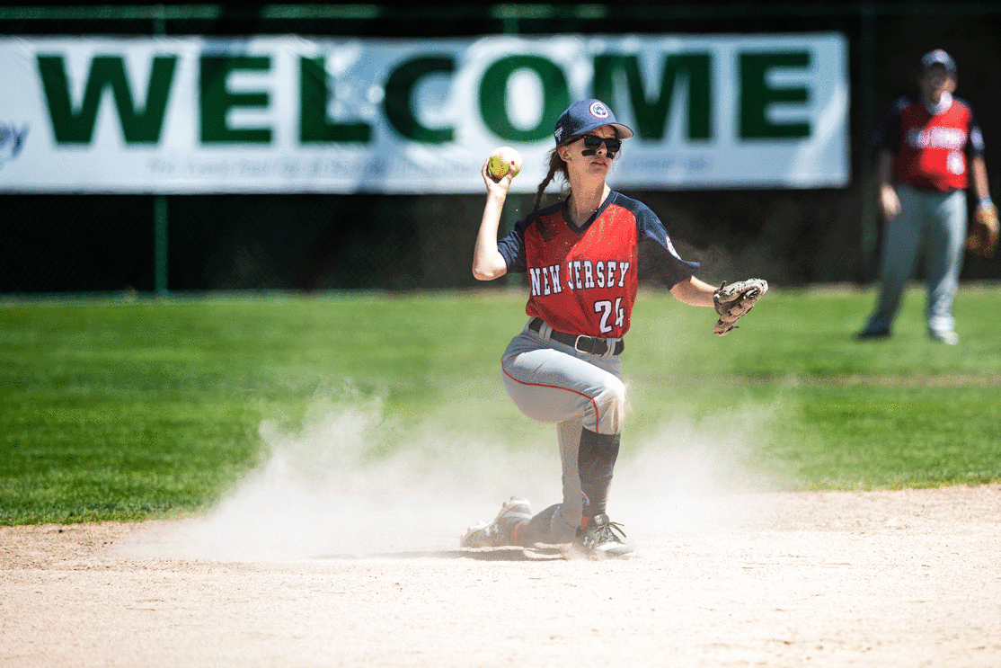 An image of a softball player on one knee. The person is throwing a ball and wearing a hat and a glove.