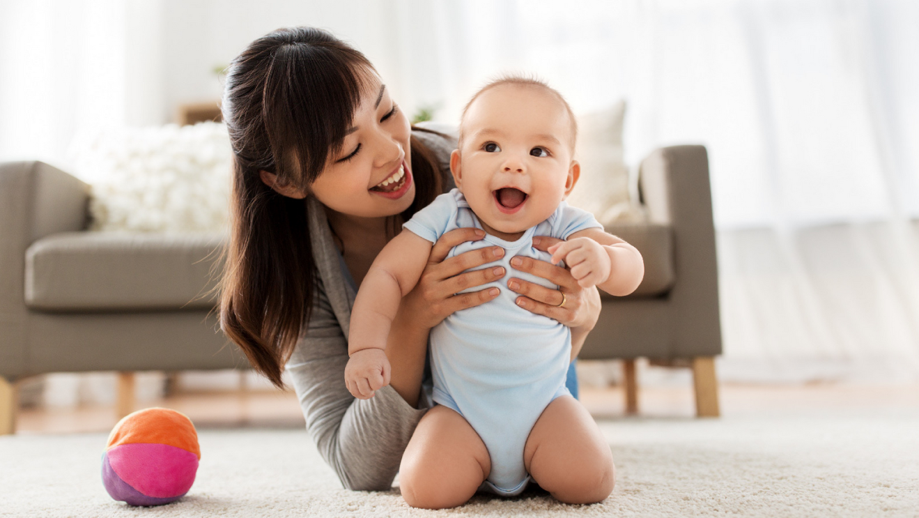 A woman holding a smiling baby in a living room