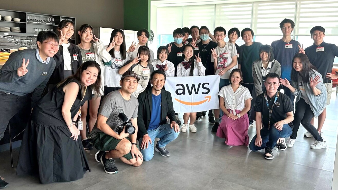 Vlogger Ghib Ojisan, Japanese high school students and Amazon staff posing with an AWS flag in the AWS Singapore office.