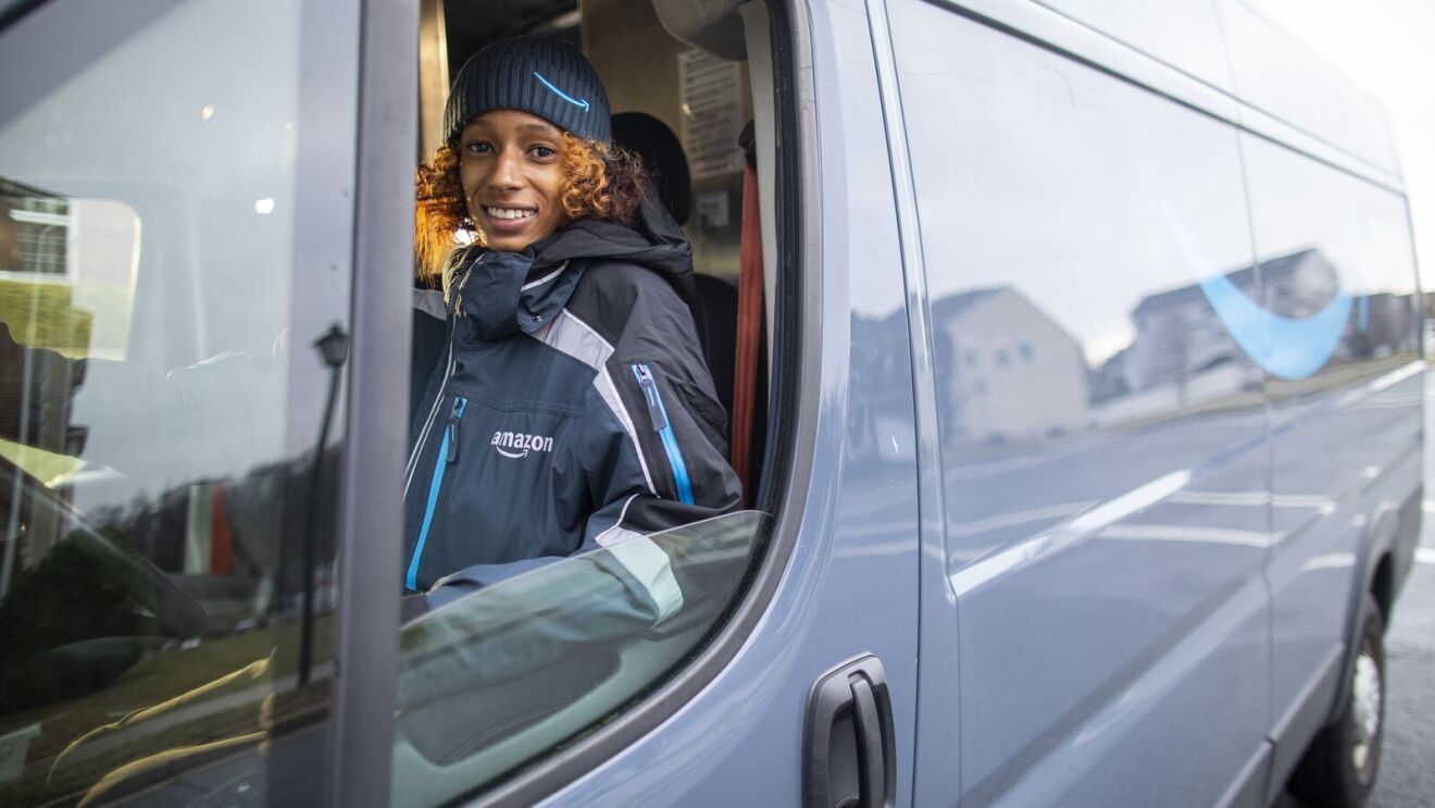 A woman wearing an Amazon hat driving an Amazon delivery van.