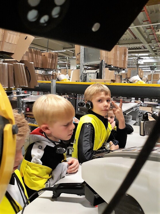 Zwei kleine Jungs in gelben Sicherheitswesten an einem Packtisch: Einer macht das Siegeszeichen