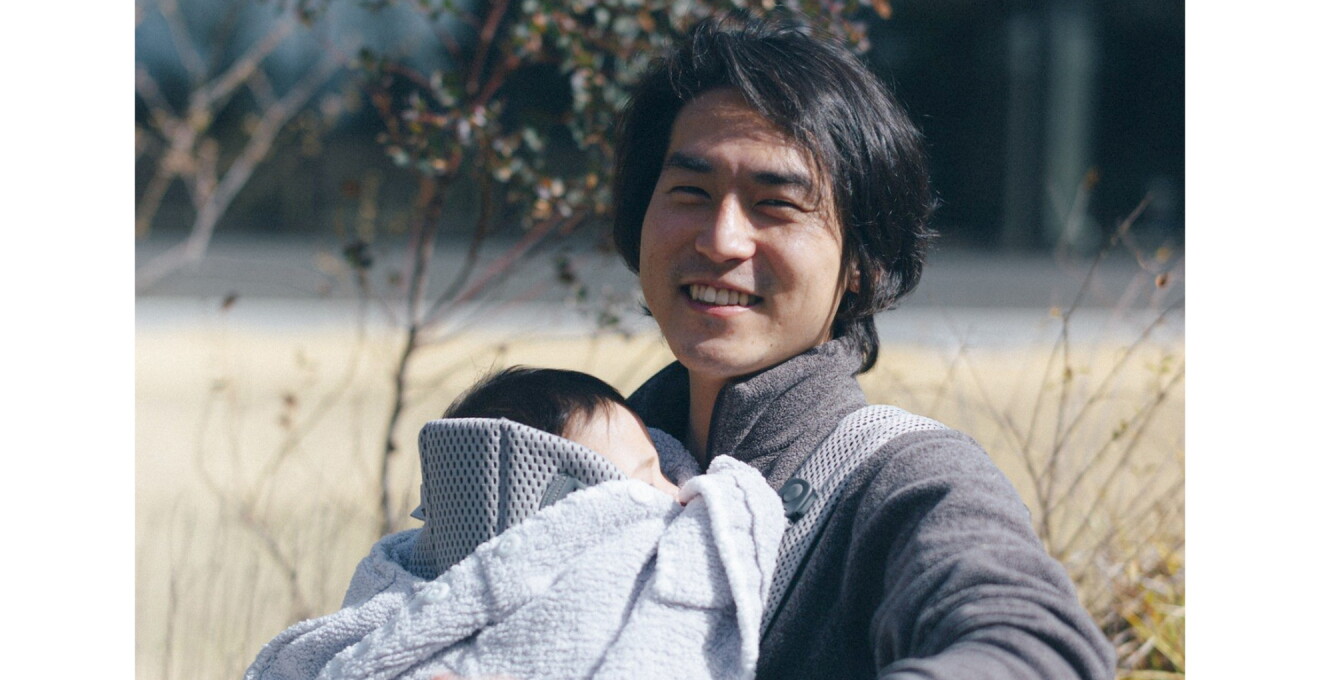 抱っこ紐でお子さんを抱く笑顔の田中さんの写真