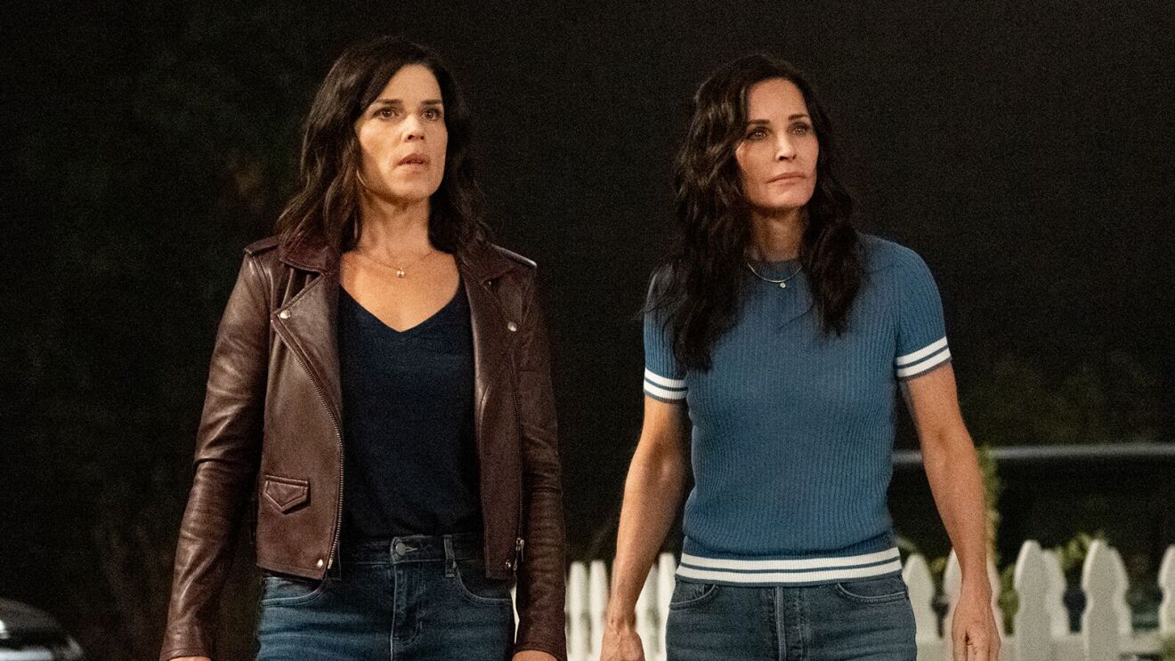Neve Campbell in leather jacket next to Courteney Cox in blue shirt outdoors at night in Scream 5