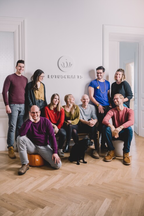 Das Team von Lotuscrafts sitzt und steht vor einer weißen Wand und lacht in die Kamera.
