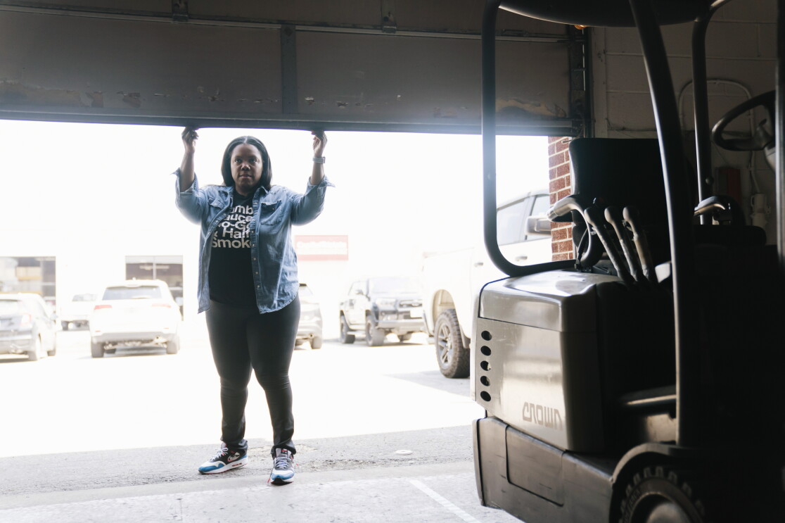 Arsha Jones opens the garage door to her warehouse where a forklift is parked.