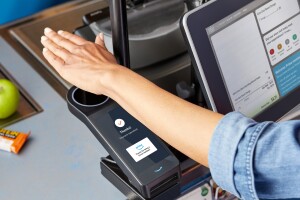 A hand hovers over a scanner at a grocery store, allowing a woman to check out and purchase her items.