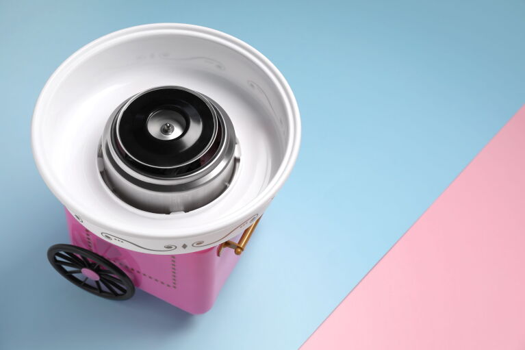 ピンク色のわたあめ機 がパステルブルーとピンクの台の上に置かれている