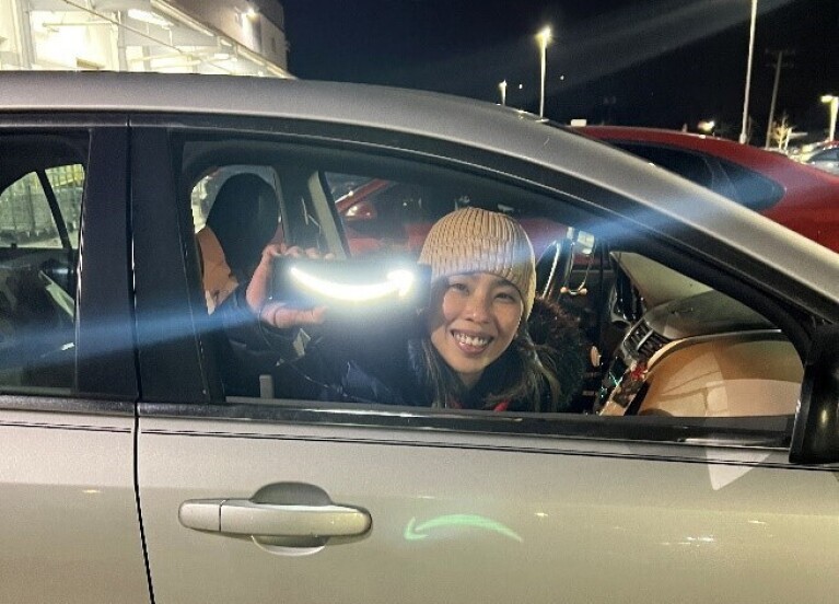 An Amazon delivery driver holds up a Amazon smile light as she sits in the driver's seat of her car.