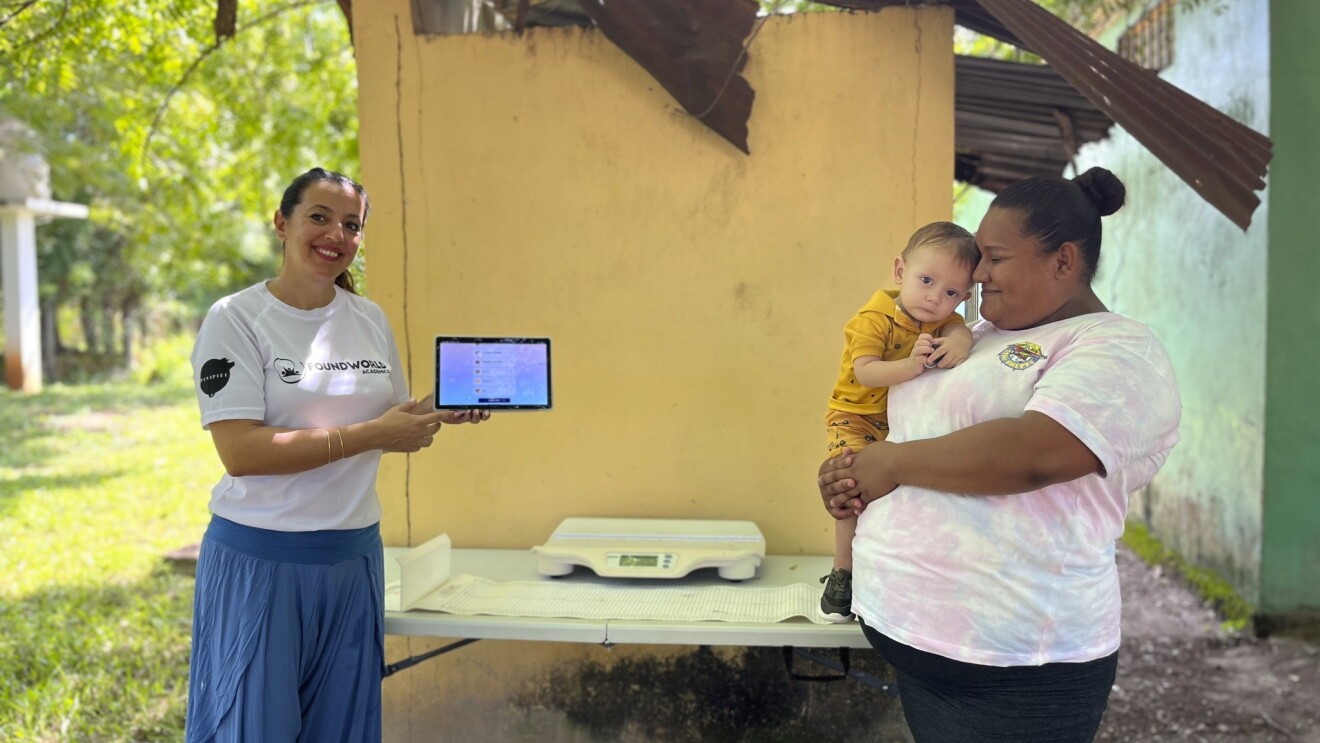 Cooperante de la Fundación Salud Infantil con una tablet delante de una madre con su hijo en brazos. 