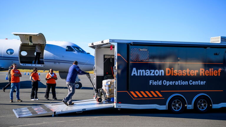 Amazon Disaster Relief trailer on tarmac with workers loading supplies from cargo plane