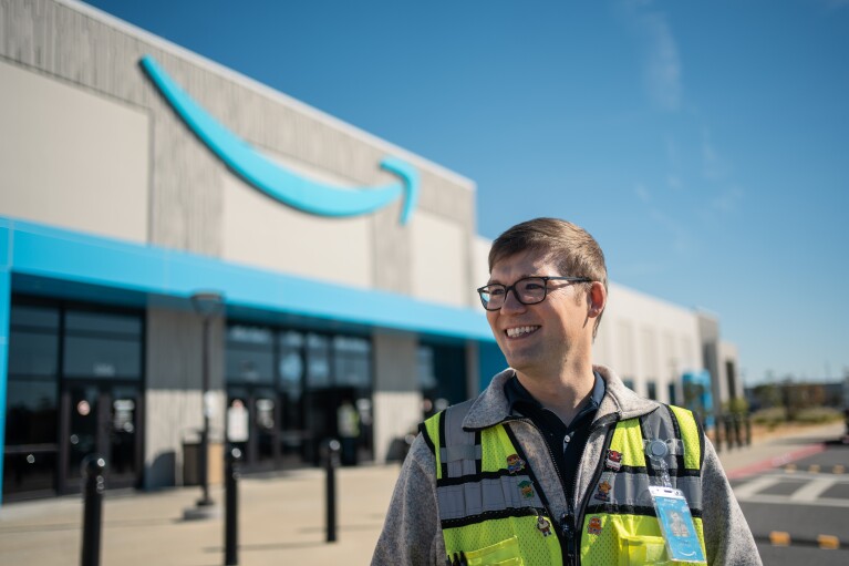 An Amazon employee stands proudly outside of a fulfillment center in a small town.
