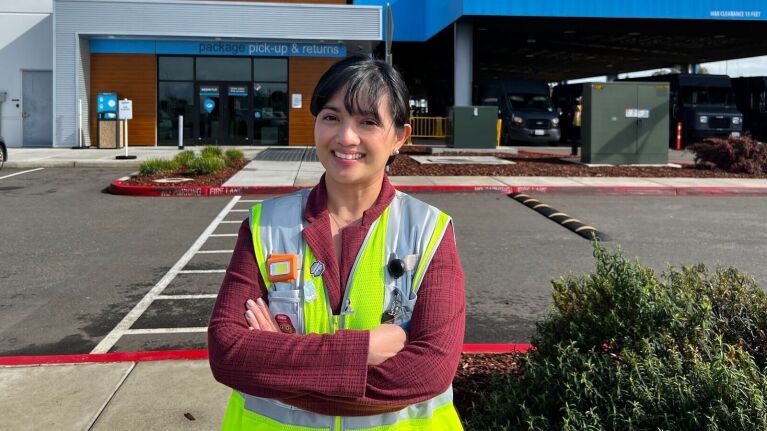 An image of a woman dressed in a yellow work vest working at an Amazon facility.