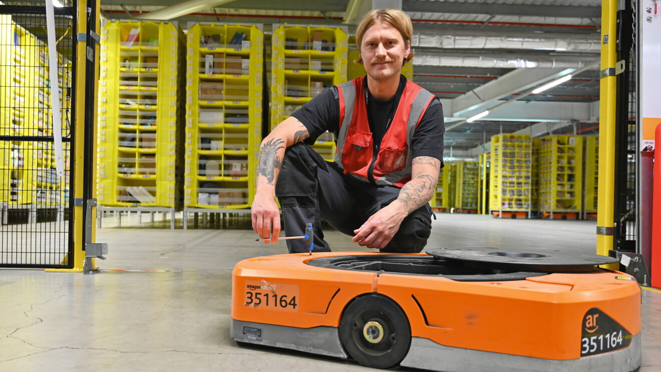 A man kneels next to an Amazon robot 